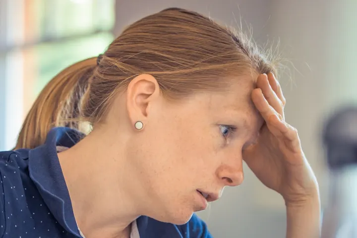 A woman at her desk with her hand on her forehead