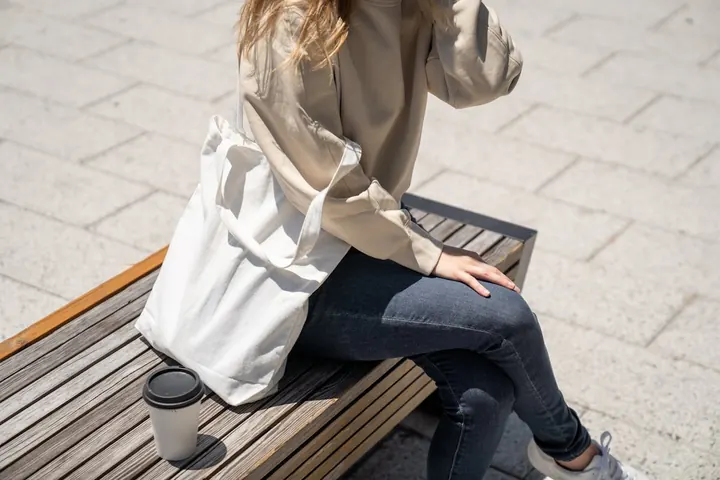 A woman sitting on a bench with a canvas tote bag