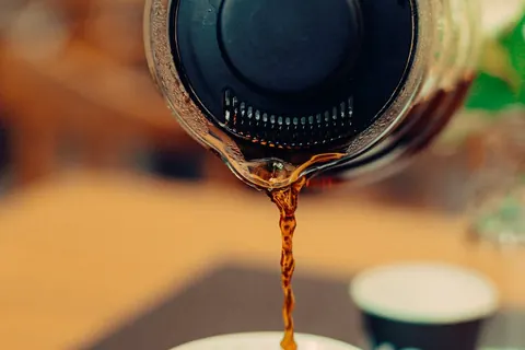 Coffee pouring from a glass carafe into a cup